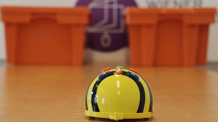 Ein Bee-Bot im Vordergrund, zwei riesengroß wirkende Digiboxen im Hintergrund