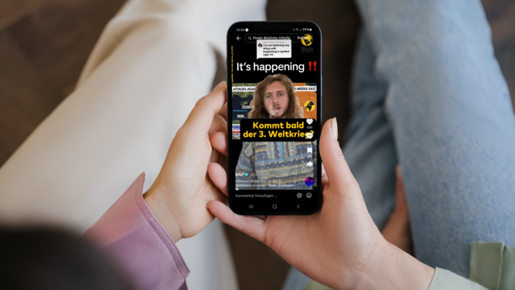 Nahaufnahme einer Person, die mit Smartphone in der Hand auf einer Couch liegt. Am Display des Smartphones ist ein TikTok-Video vom Kanal Bait mit der Überschrift "Kommt bald der 3. Weltkrieg?" zu sehen.
