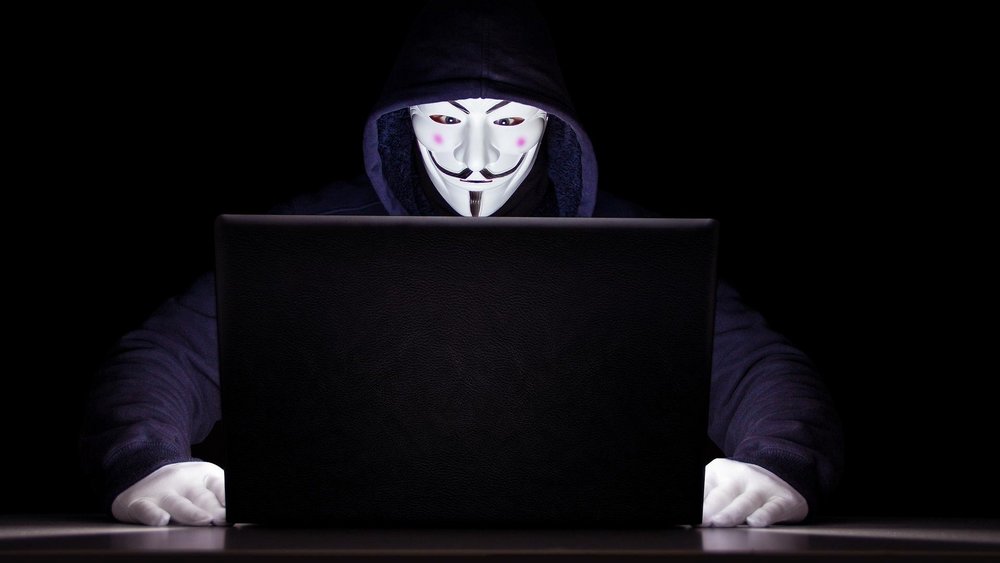 Ein Mensch mit Maske vor einem ihn anleuchtenden Laptop-Bildschirm