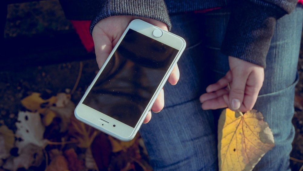 Zwei Kinderhände sind zu sehen, in einer Hand wird ein Smartphone gehalten, in der anderen ein Blatt.