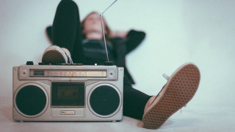 Im Vordergrund steht ein Radio, dahinter liegt entspannt ein junger Mensch und hört zu.