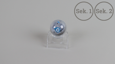 Ein Foto des Sphero Mini Roboters auf transparenter Halterung. Rechts oben steht "Sek. 1" und "Sek. 2".