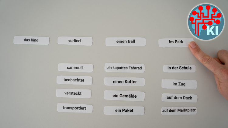 Foto verschiedener, nebeneinander liegender Papierschnipsel, auf denen Worte zu lesen sind. Diese ergeben den Satz "Das Kind verliert einen Ball im Park.". Ein Finger zeigt auf einen Schnipsel.