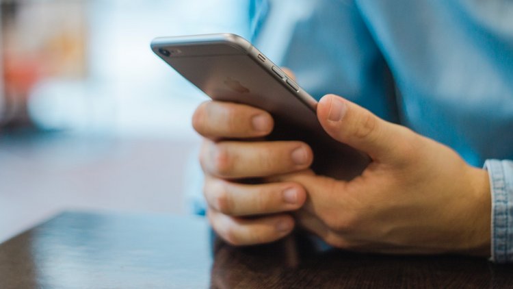 Nahaufnahme von zwei Händen, die ein iPhone halten.