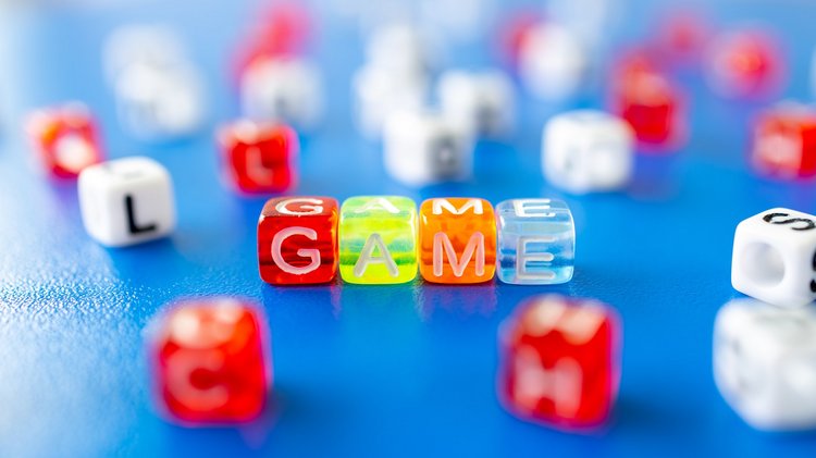 Verschiedene bunte Würfel liegen auf einer blauen Oberfläche, 4 Würfel bilden das Wort "Game".