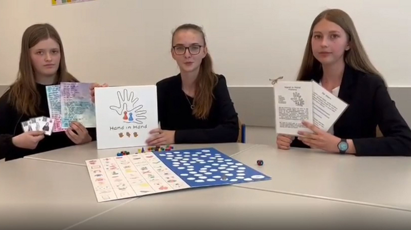 Drei Schülerinnen präsentieren das inklusive Brettspiel "Hand in Hand" zum Erlernen der Gebärdensprache